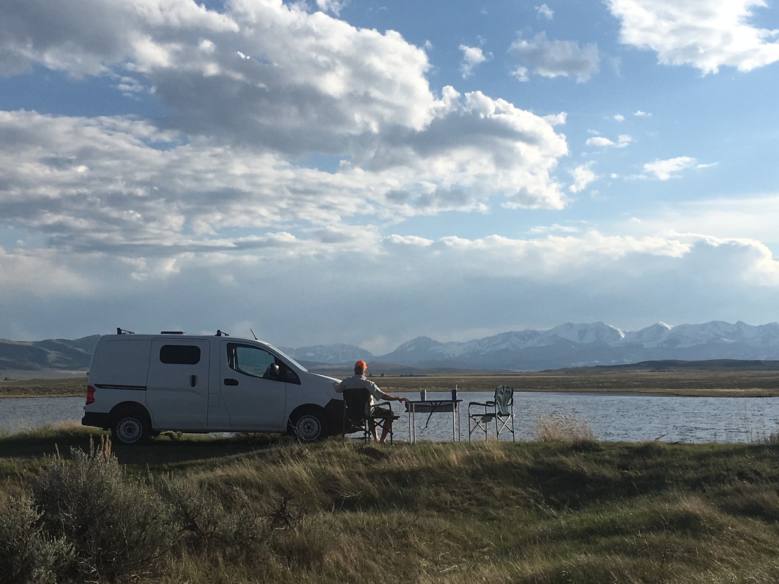 facing snow-capped mountains under blue sky. Ideal RV rental for scenic adventures.|Relaxing by the water in an RV rental