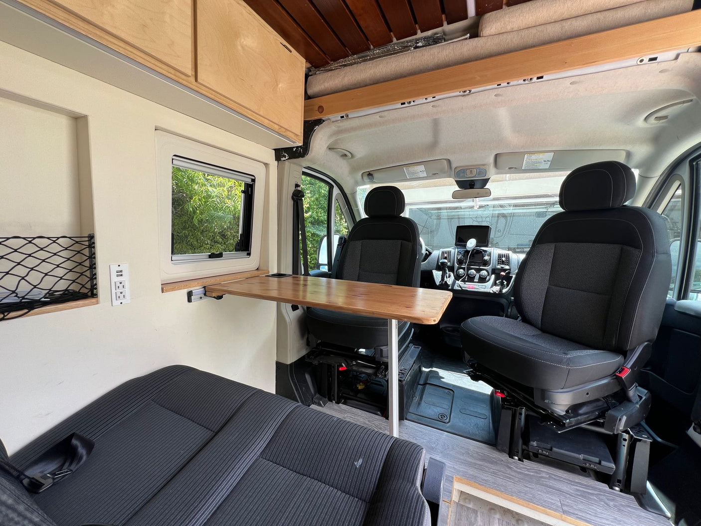 Inside an RV rental, showcasing the front cab's swivel seats, functional wooden table, and cozy living area with storage.