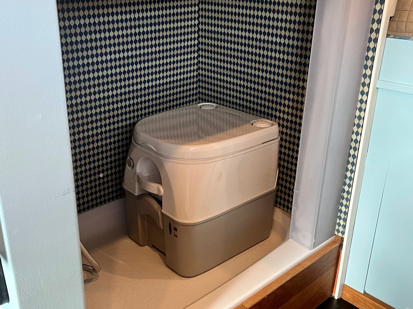 Inside an RV rental: a portable toilet sits in a small, patterned nook with blue geometric wallpaper and a shower curtain.
