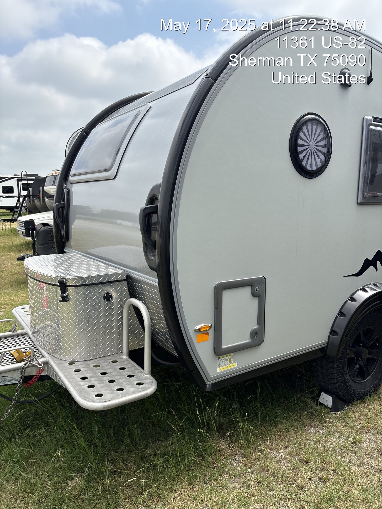 A modern teardrop camper, perfect for an RV rental adventure, parked on grass at a campsite.