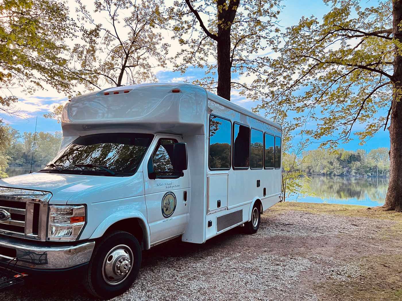 White RV rental for nature therapy parked by a reflective lake, surrounded by fresh green trees. Peaceful outdoor setting. — photo 10