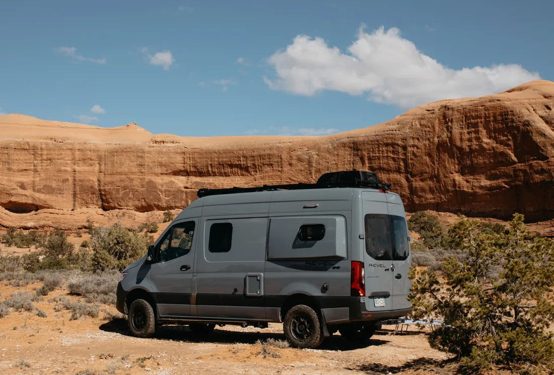 Grey Winnebago Revel 4x4 RV rental parked in a desert landscape with orange rock formations. Perfect for off-road adventure.
