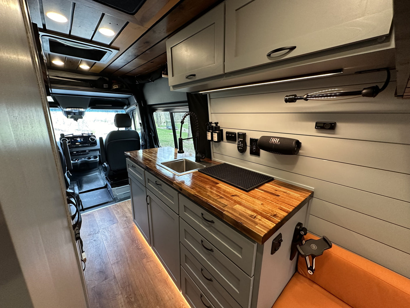 Bright RV rental interior: modern kitchen with wood counters, sink, cabinets, and ambient lighting. Perfect for your next camper van adventure.