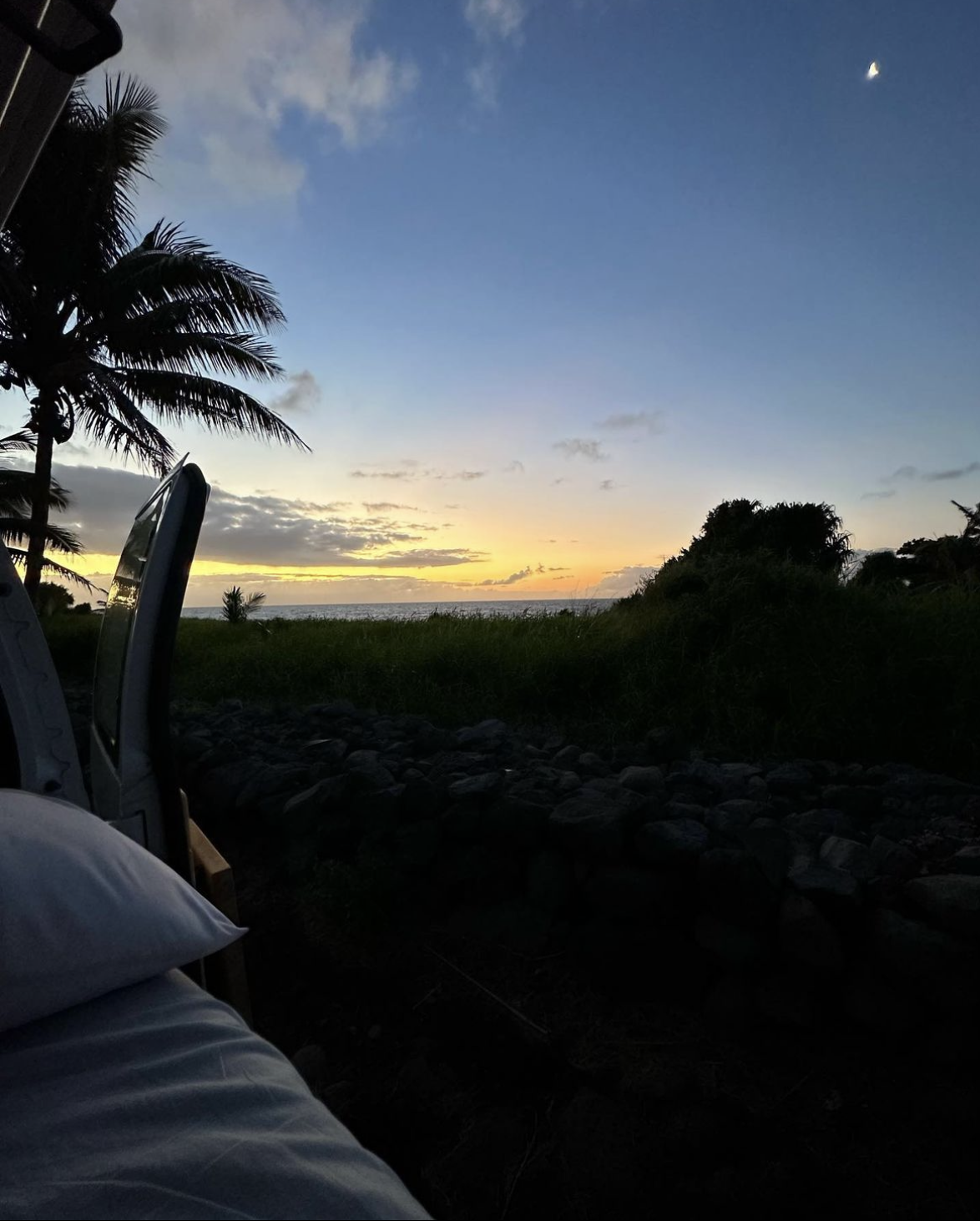 Inside our RV rental, an open door frames a calming ocean sunset. Palm trees and the moon complete this perfect travel view.