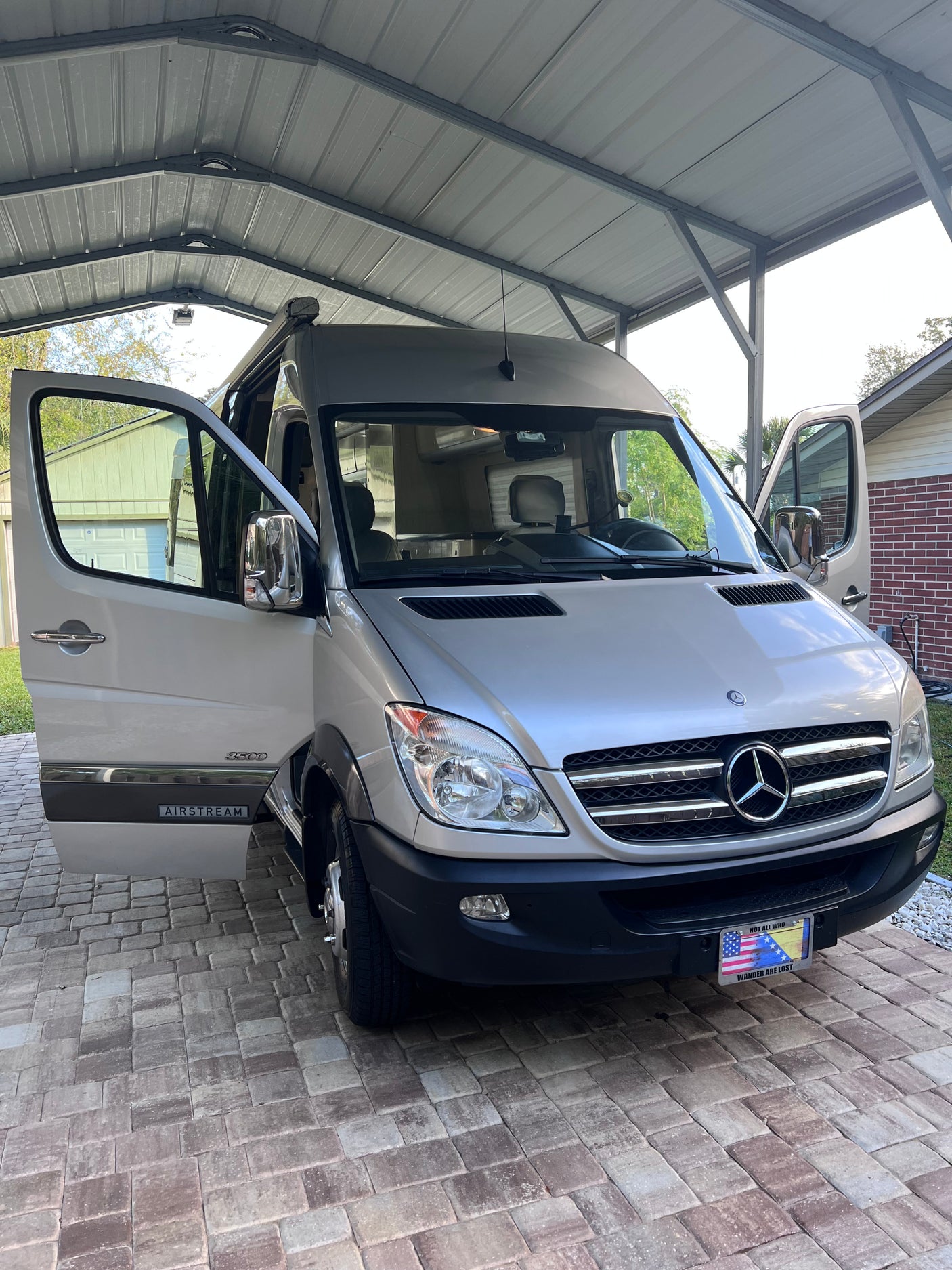 Silver Airstream Mercedes Sprinter RV rental camper van parked under a carport with doors open on pavers.