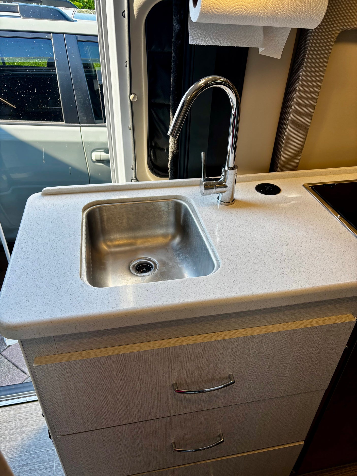 RV rental kitchen: modern galley with stainless steel sink, chrome faucet, speckled countertop, and light wood-grain drawers.