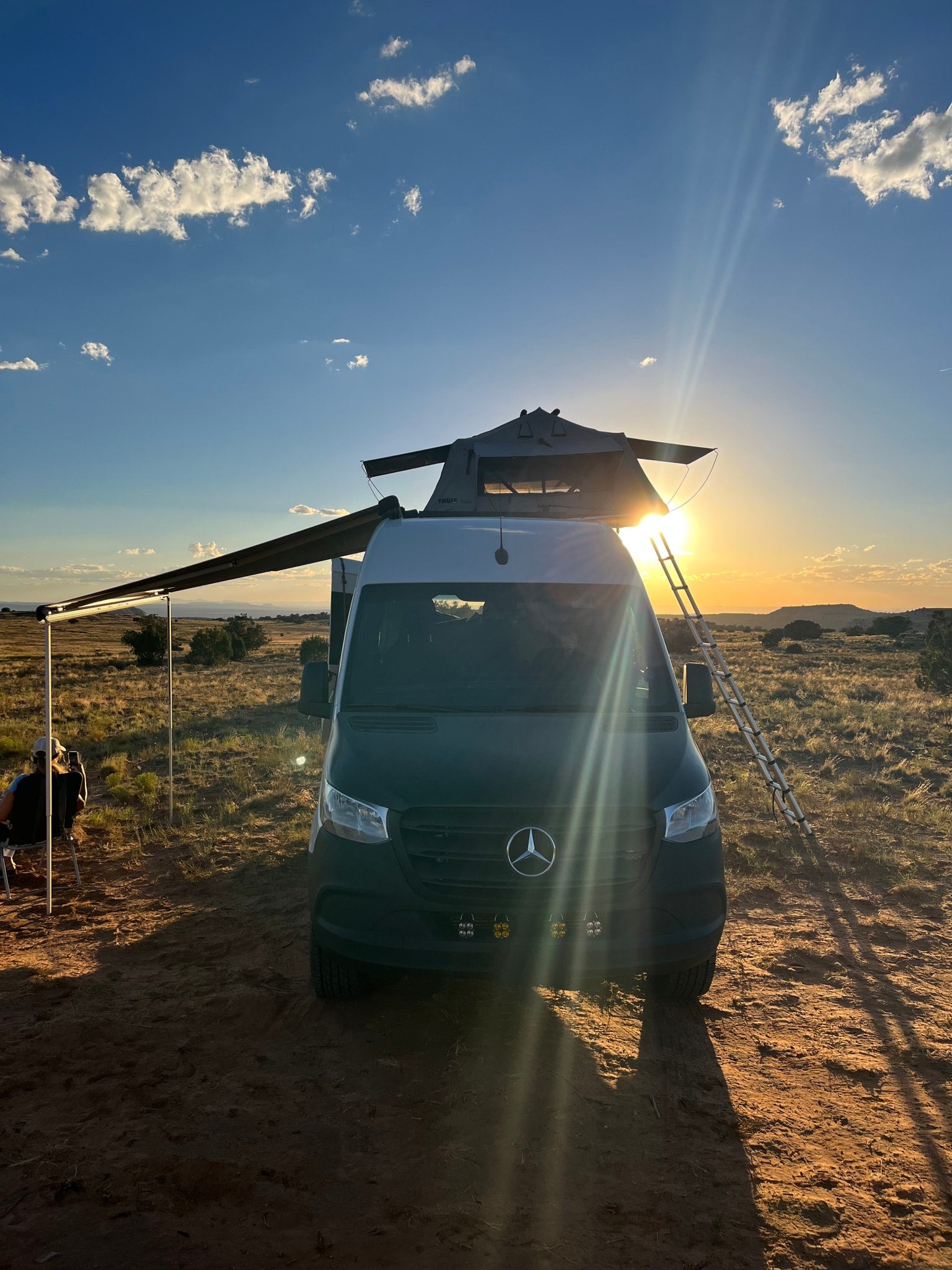 Off-grid RV rental: Mercedes Sprinter van, rooftop tent, and awning during a beautiful desert sunset.