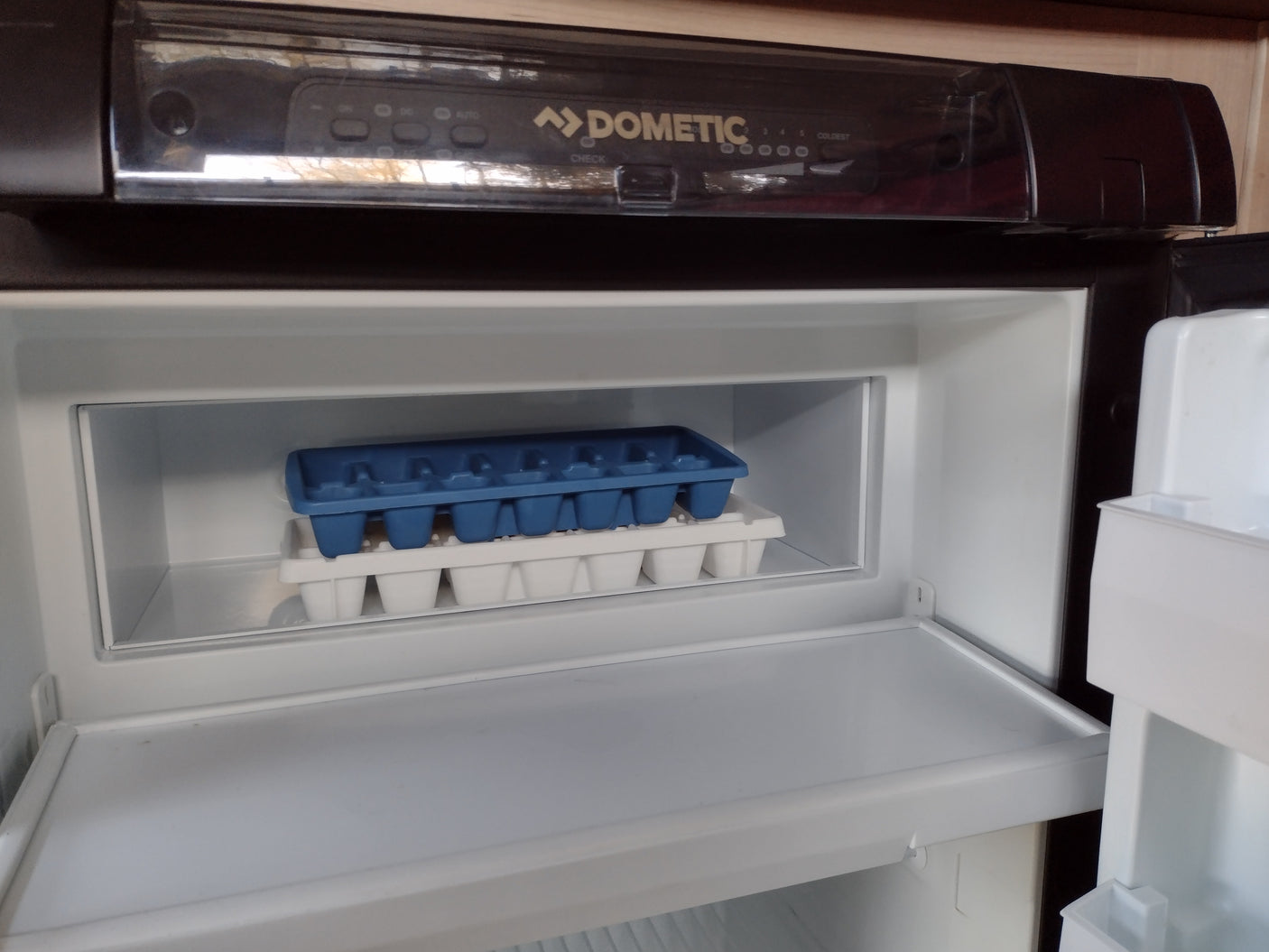 Clean Dometic RV refrigerator with empty blue & white ice trays, ideal for your next RV rental adventure, ready for provisions.