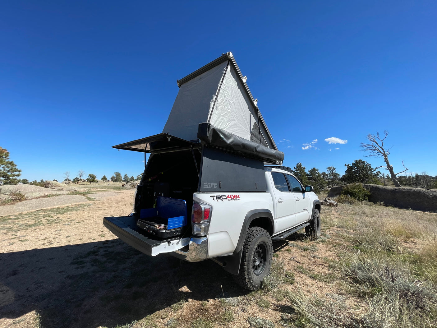 White Toyota Tacoma with pop-up camper, equipped for RV rental. Ready for overlanding & wilderness camping with cooking gear.