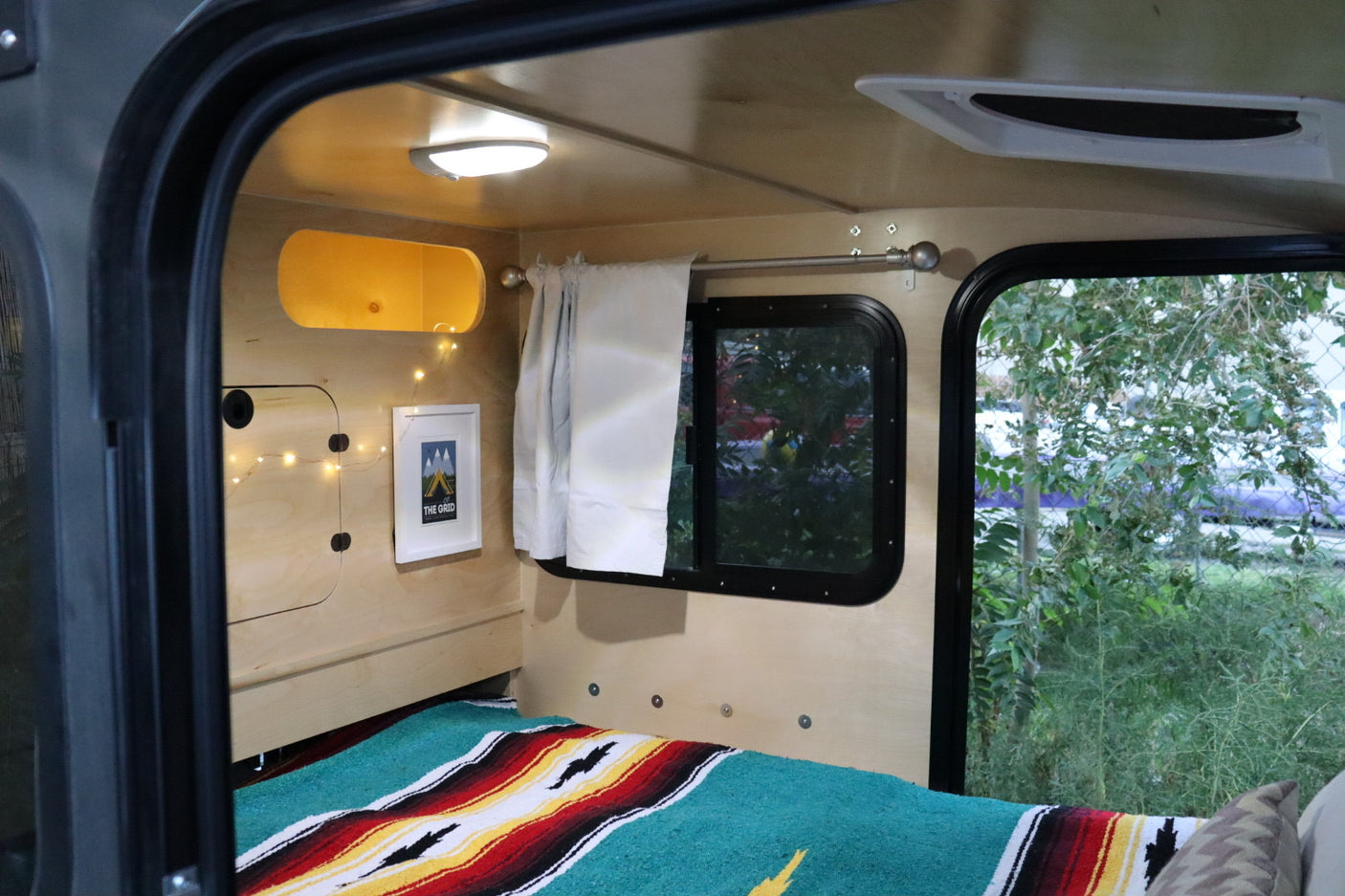 Inside a cozy RV rental: a comfortable bed with colorful blanket, window views, and warm lighting, perfect for travel.