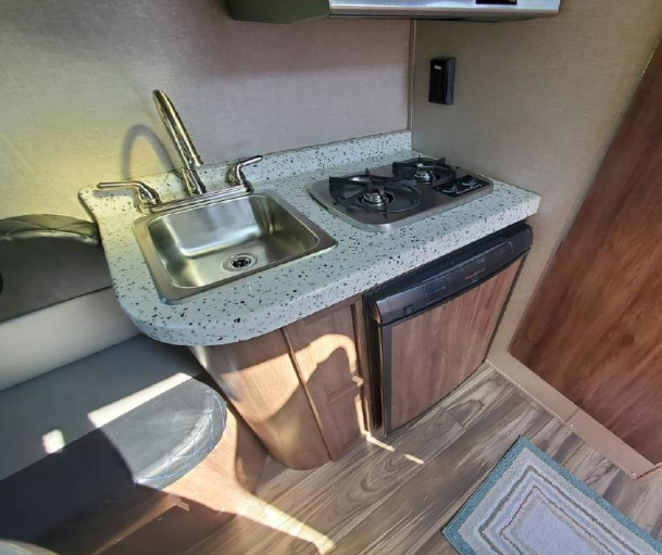 Inside an RV rental: a practical kitchenette with sink, two-burner stove, and compact fridge.