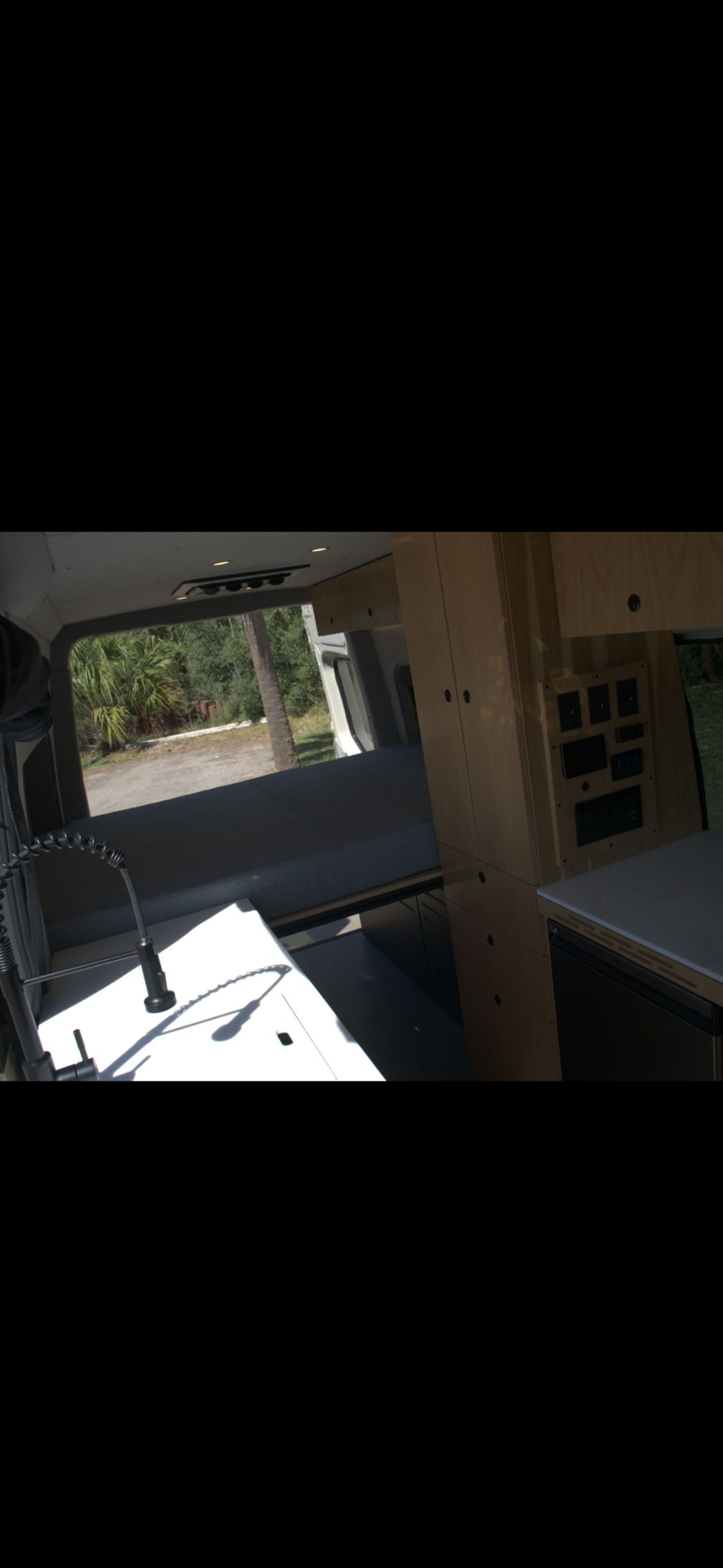 Inside this rv rental, a camper van features a kitchenette with a pull-down faucet, a sleeping area, wood cabinets, and an electrical control panel.