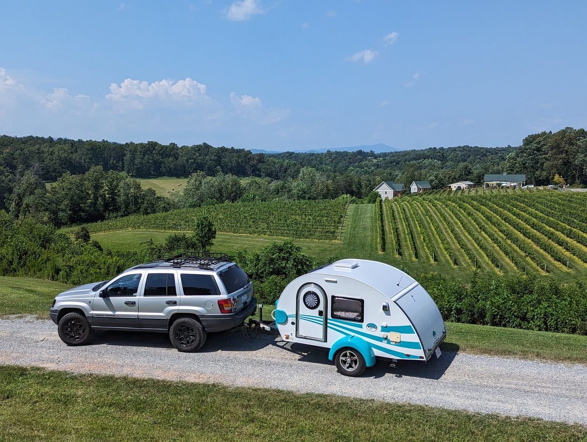Scenic vineyard view! Silver SUV towing a white teardrop camper, perfect for an rv rental road trip. Green hills & blue sky. — photo 18