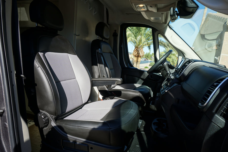 Spacious RV rental interior with driver & passenger seats, dashboard, and a sunny palm tree view.
