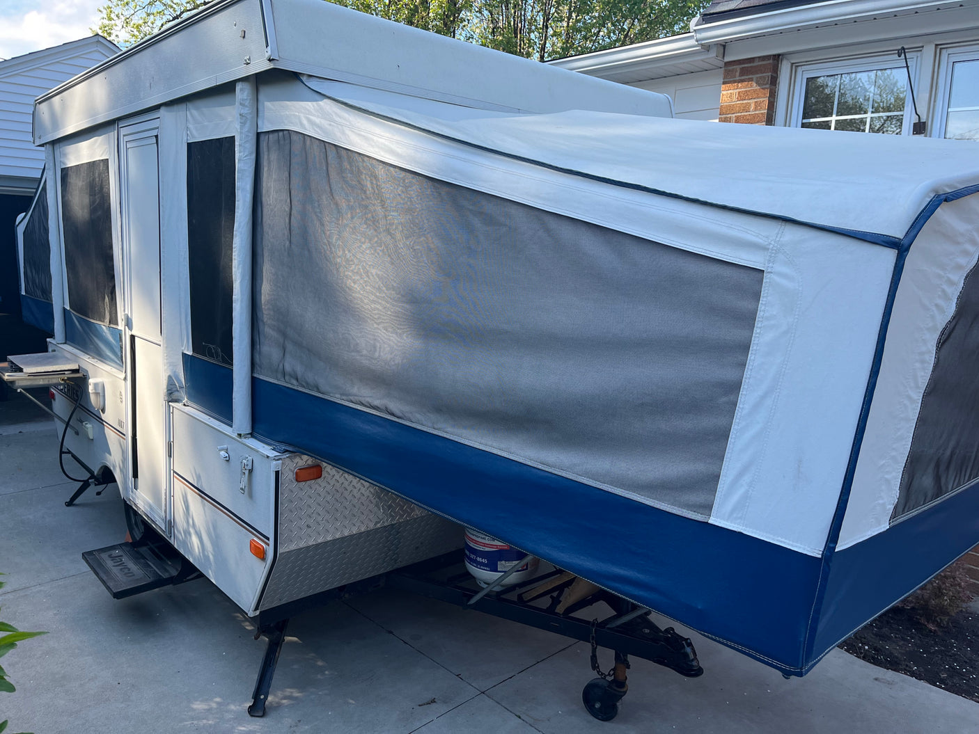 This white and blue pop-up camper, ideal for an RV rental, is fully set up with mesh windows, ready for outdoor adventures.