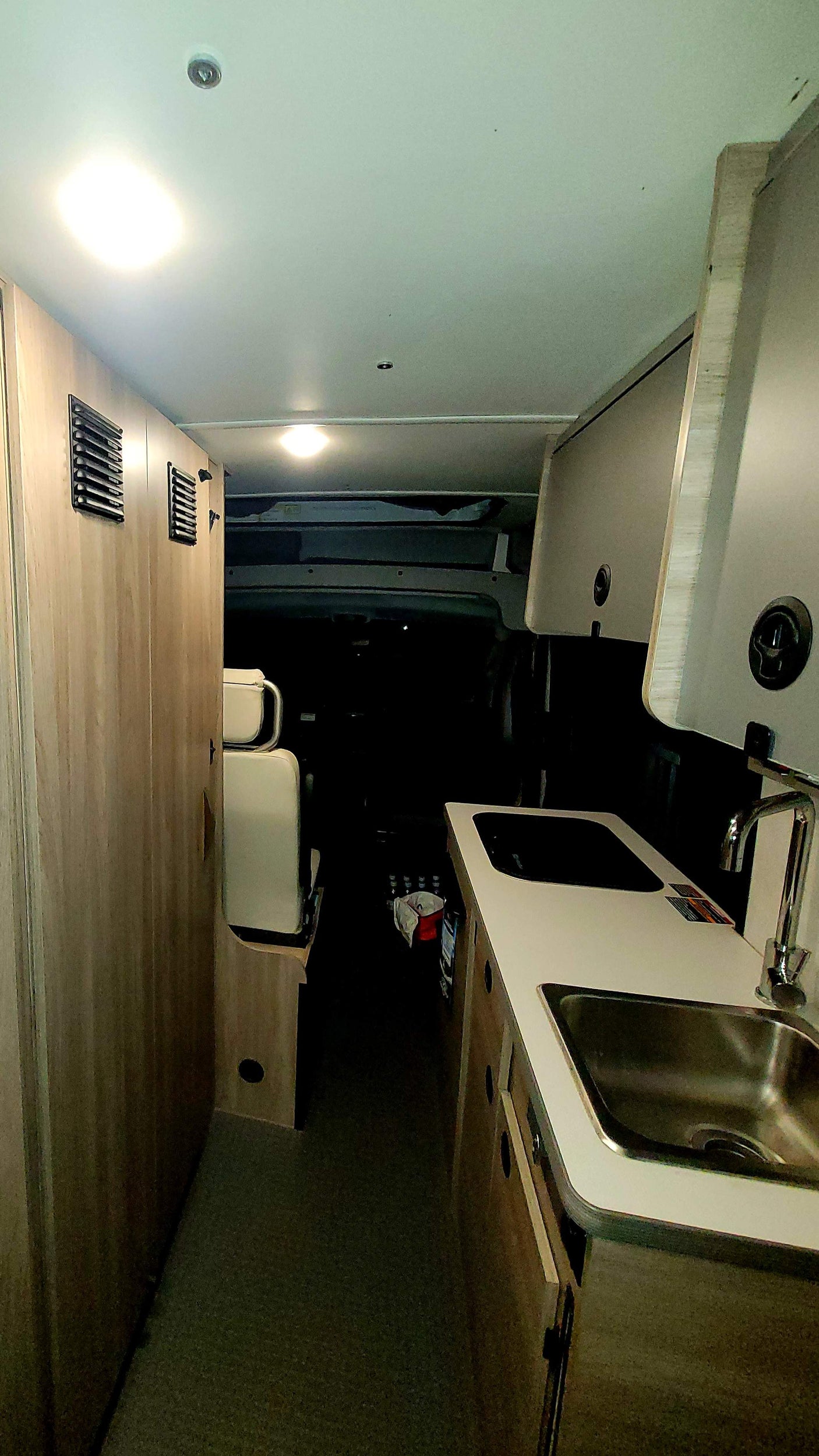 This RV rental interior features a compact kitchenette with a sink and stovetop on the right, opposite light wood cabinetry.
