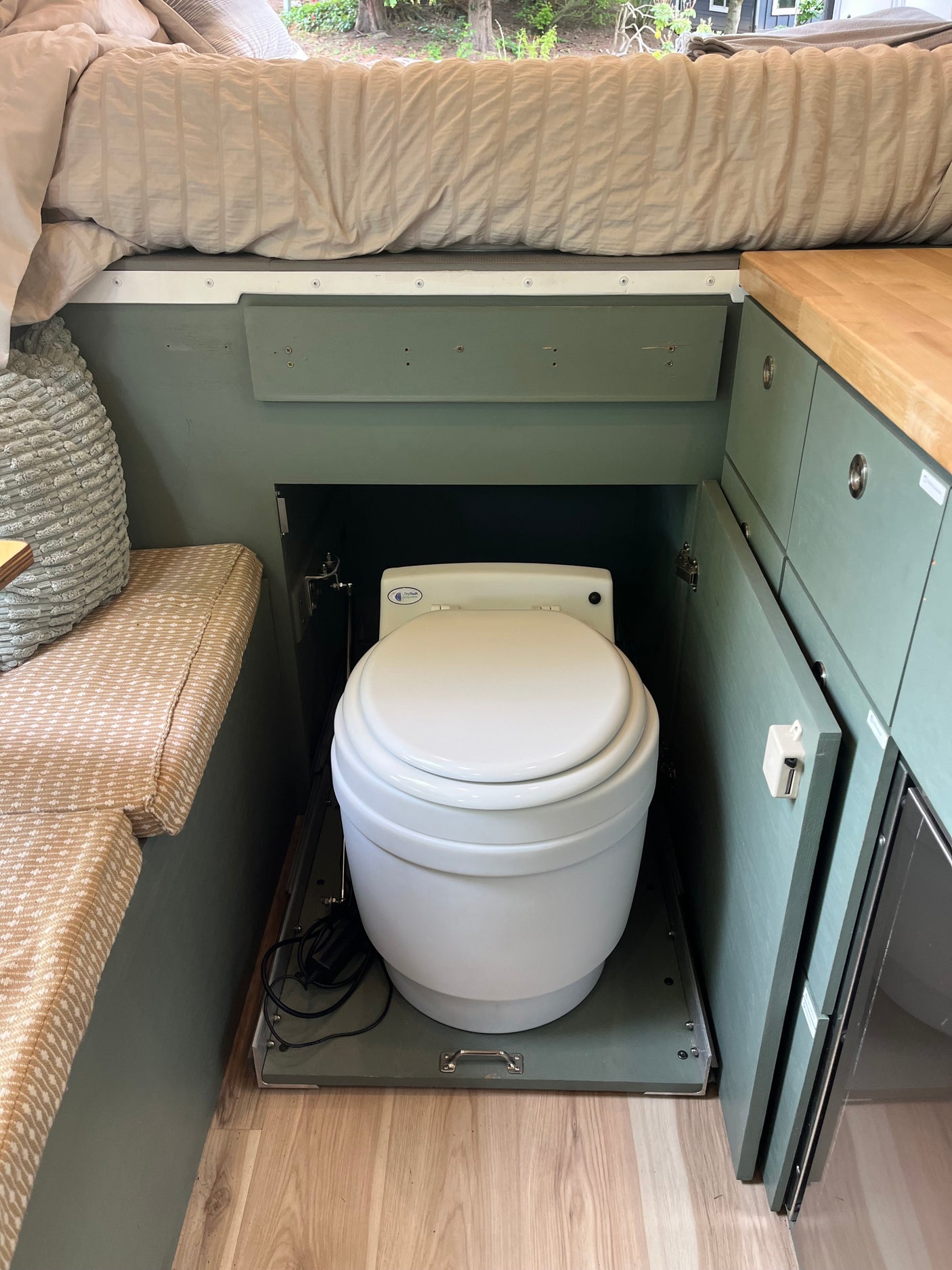 Compact RV rental features a hidden composting toilet on a pull-out base, maximizing space under the bed.