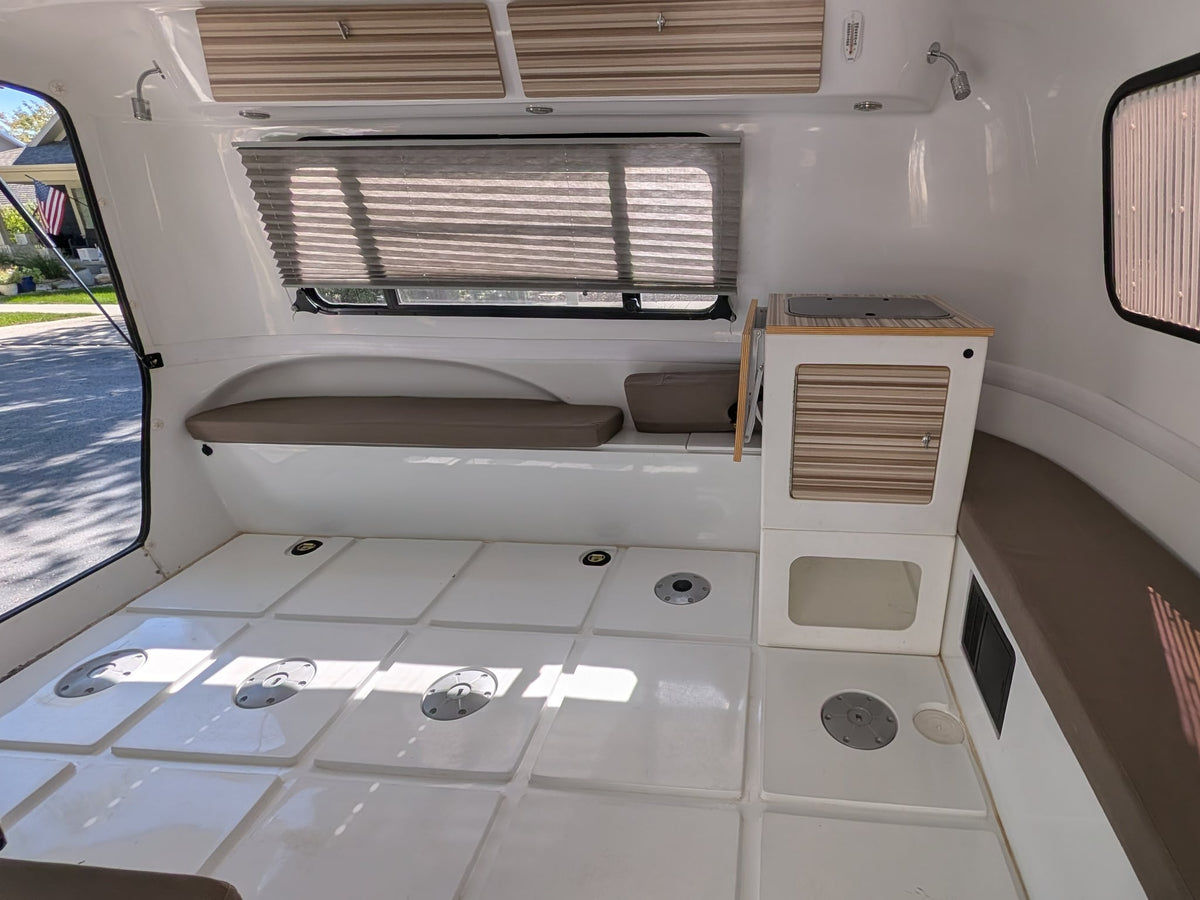 and a collapsible dining table.|Compact RV rental interior featuring a convertible bed/seating area and a small kitchenette with striped cabinets.|RV rental teardrop camper set up with a privacy tent — photo 10
