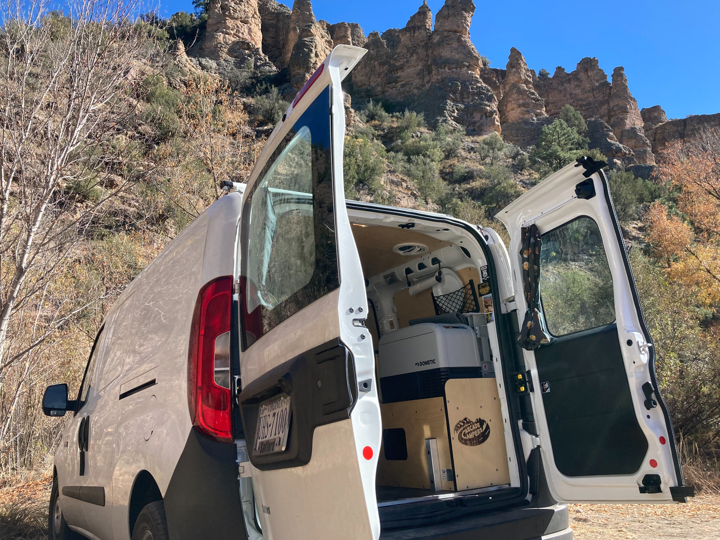 White camper van rv rental, doors open, reveals its Dometic cooler. Perfect for mountain adventure & van life in rugged nature.