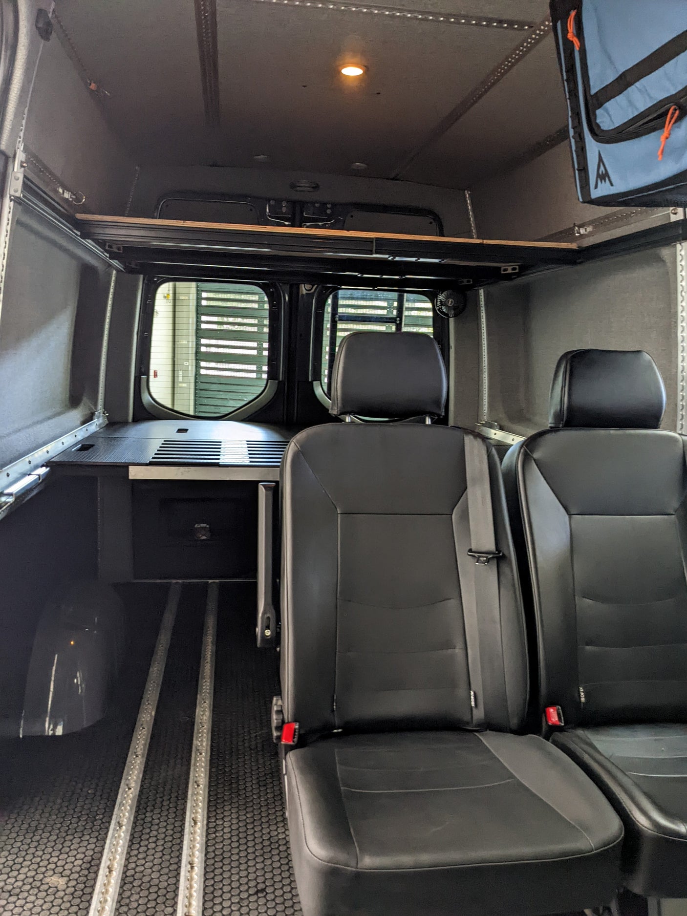 RV rental interior: black passenger seats, floor tracks, and a compact utility counter for versatile travel.