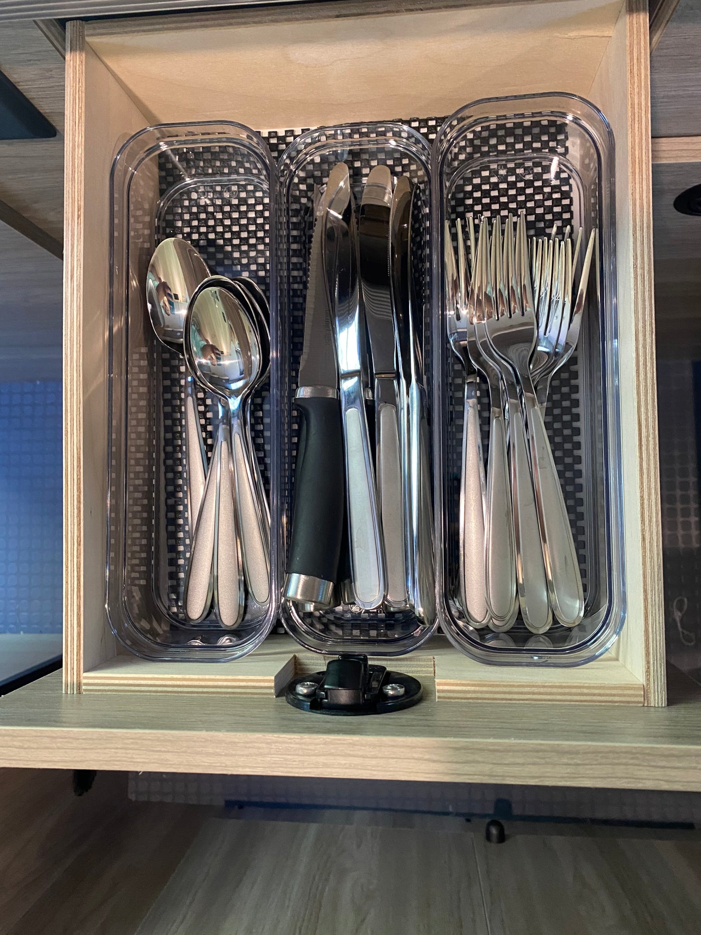 RV rental: Organized kitchen drawer with silver spoons, knives, & forks in clear plastic organizers on a checkered mat.