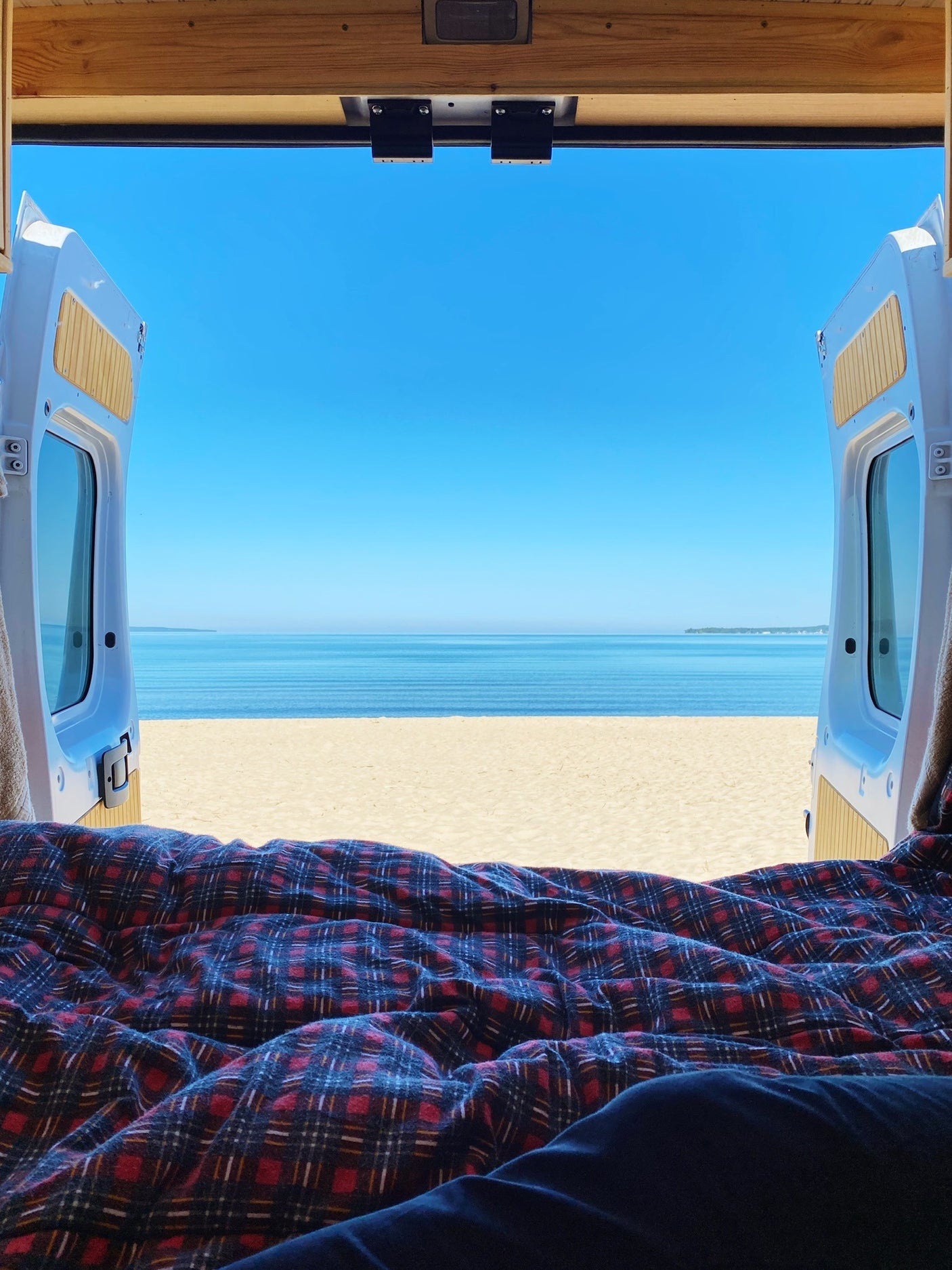 RV rental: View from inside, legs under plaid blanket, open van doors reveal beach & ocean.