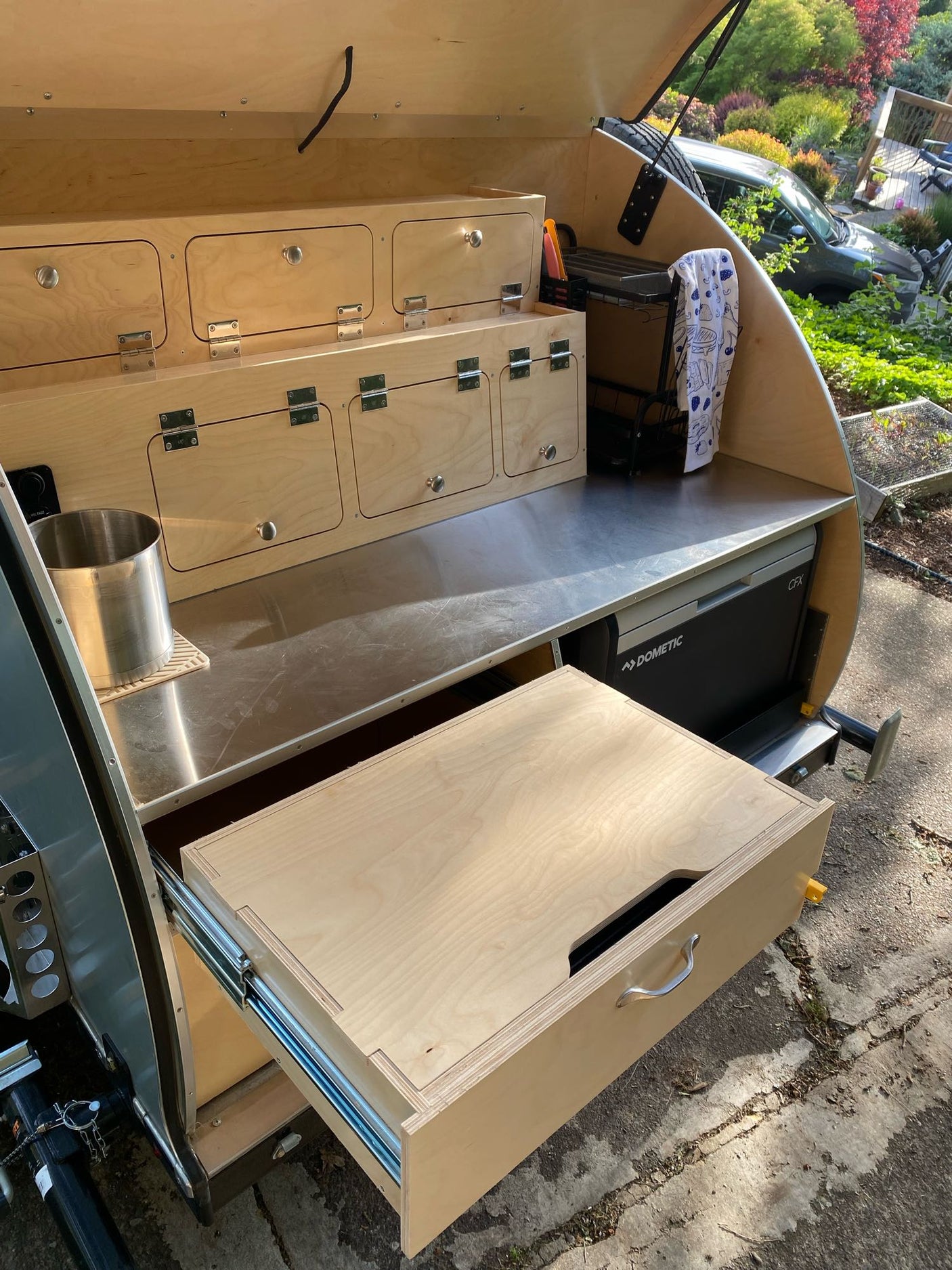 A compact RV rental's outdoor galley: custom wood cabinets, stainless counter, pull-out fridge, and ample storage for camping.