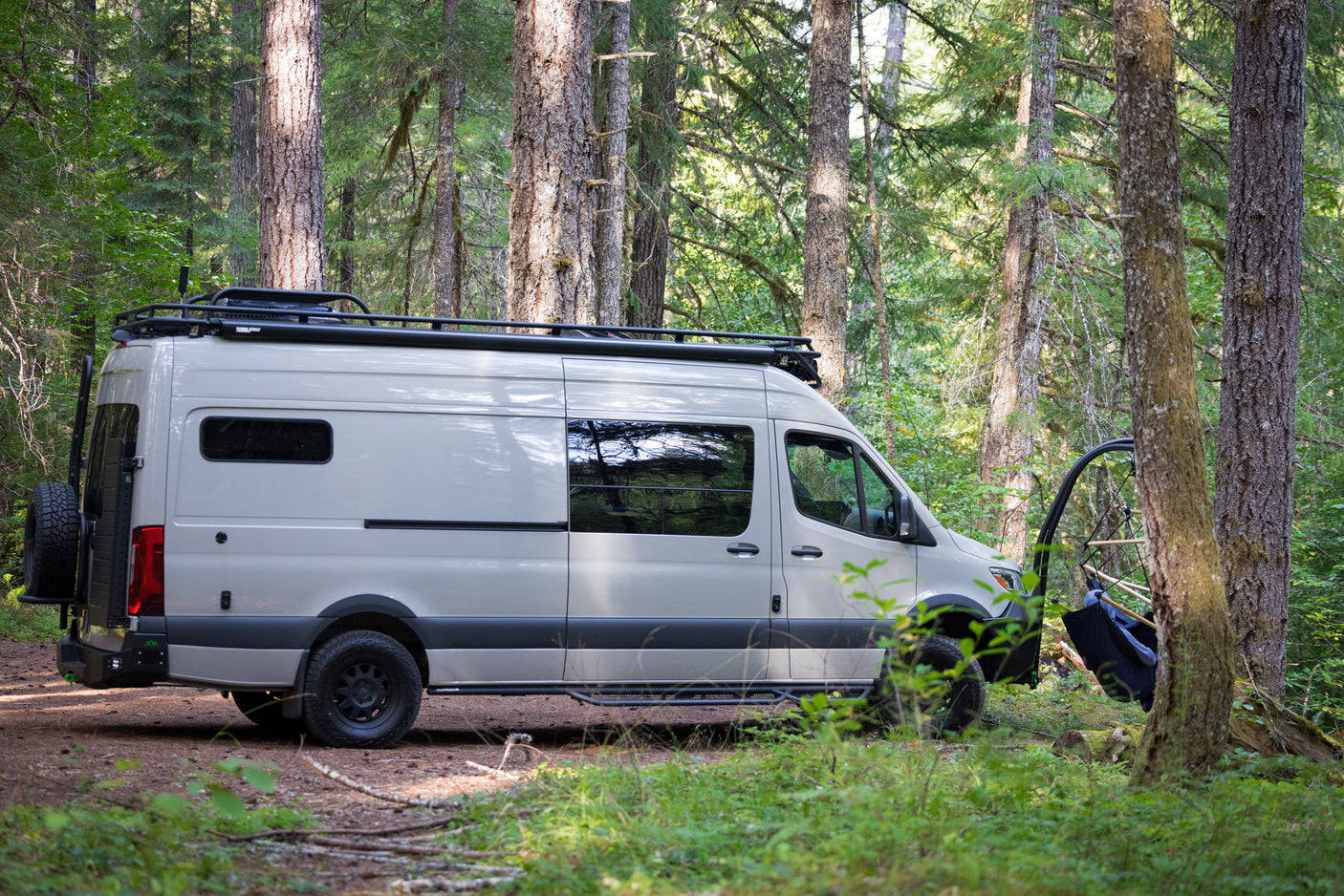 RV rental camper van parked in a lush forest with an open side door revealing a hanging chair. Ready for adventure.