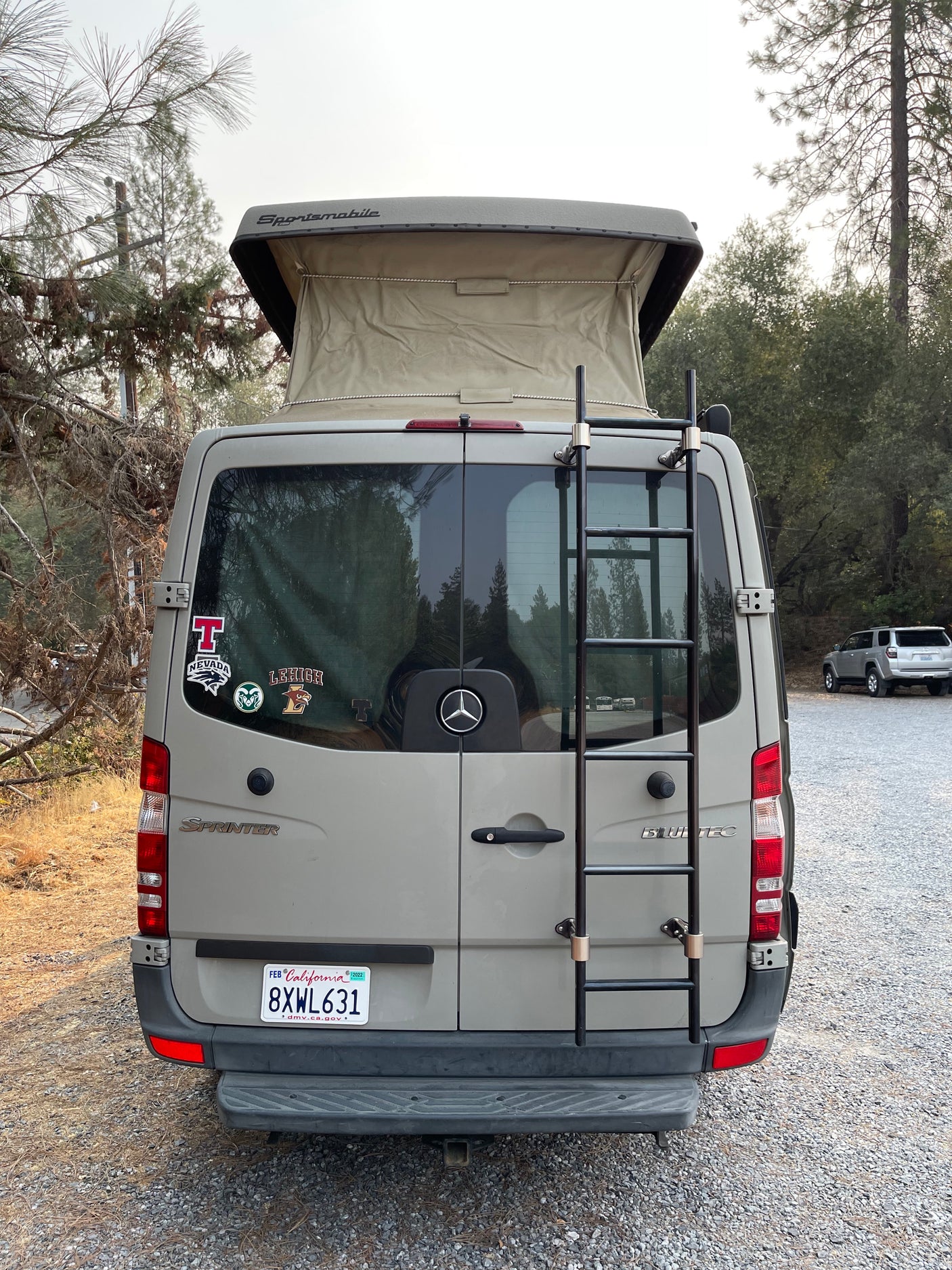 An rv rental Sprinter van featuring a pop-top roof and ladder, ideal for camping and outdoor adventures.