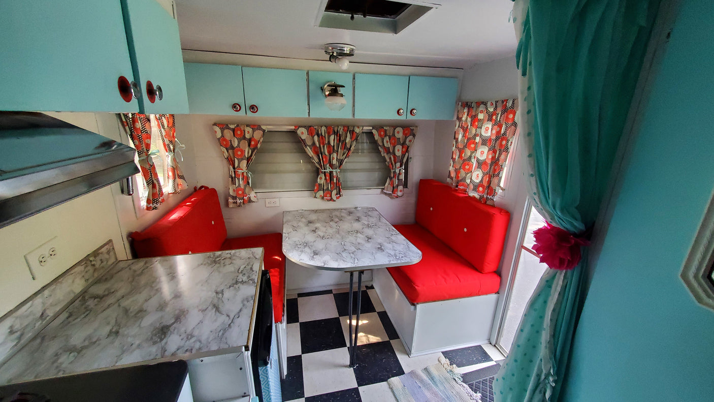 Vibrant RV rental's retro interior: turquoise cabinets, red diner-style booth, and checkered floor.