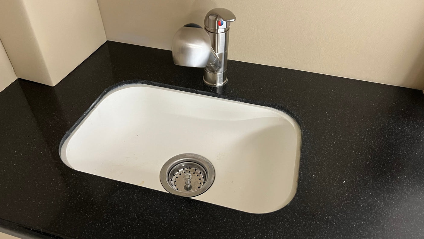 A sleek, compact sink with a modern faucet and soap dispenser on a dark countertop in an rv rental.