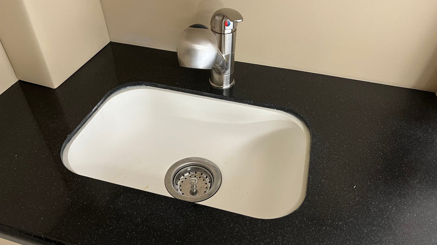 A sleek, compact sink with a modern faucet and soap dispenser on a dark countertop in an rv rental.
