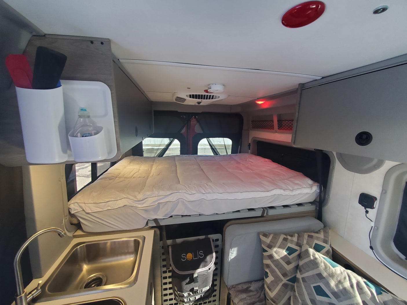 Inside an RV rental featuring a comfy bed, kitchen sink, overhead storage, and geometric pillows.