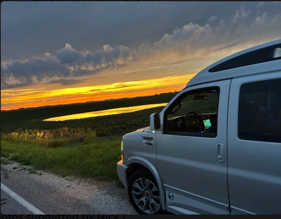 A silver conversion van by a serene mountain lake on a cloudy day