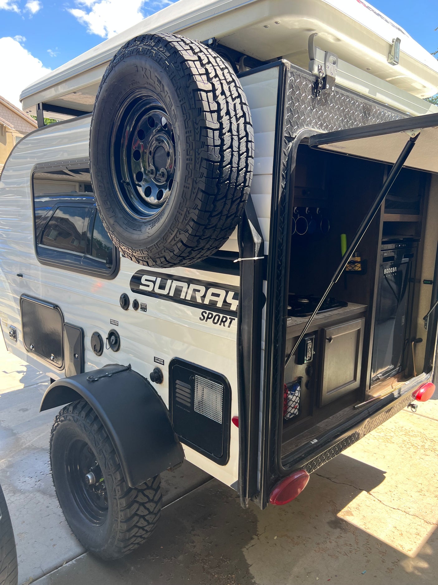 White Sunray Sport teardrop camper RV rental with an open outdoor kitchen at the rear and a rooftop tent.