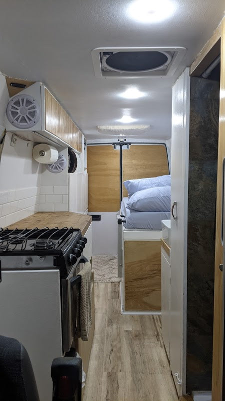 Inside a neat rv rental: compact kitchen with stove, wooden counters, a comfortable bed, and wood flooring.