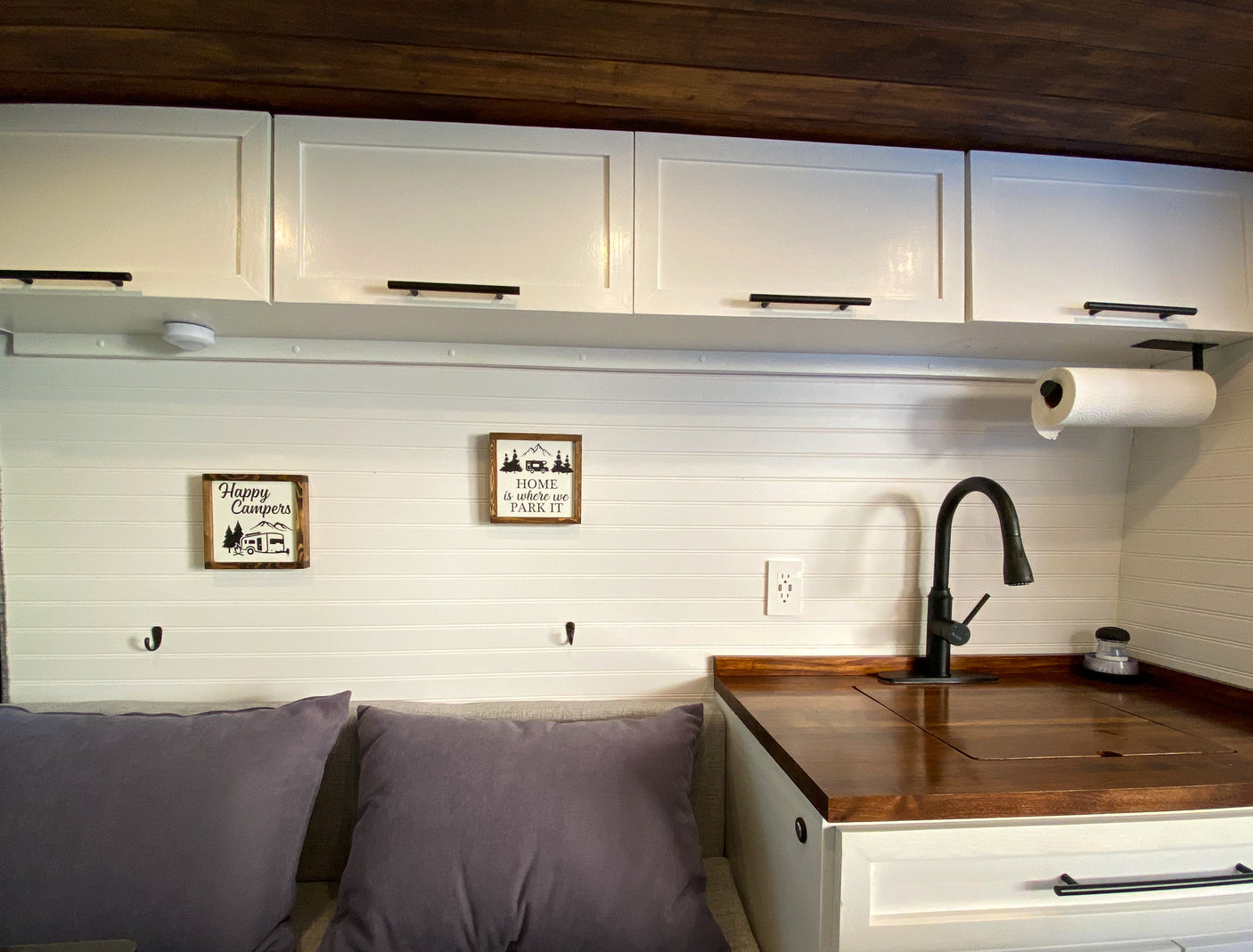 Cozy RV rental interior featuring white cabinets, wood countertop, and "Happy Campers" decor for a comfortable stay.