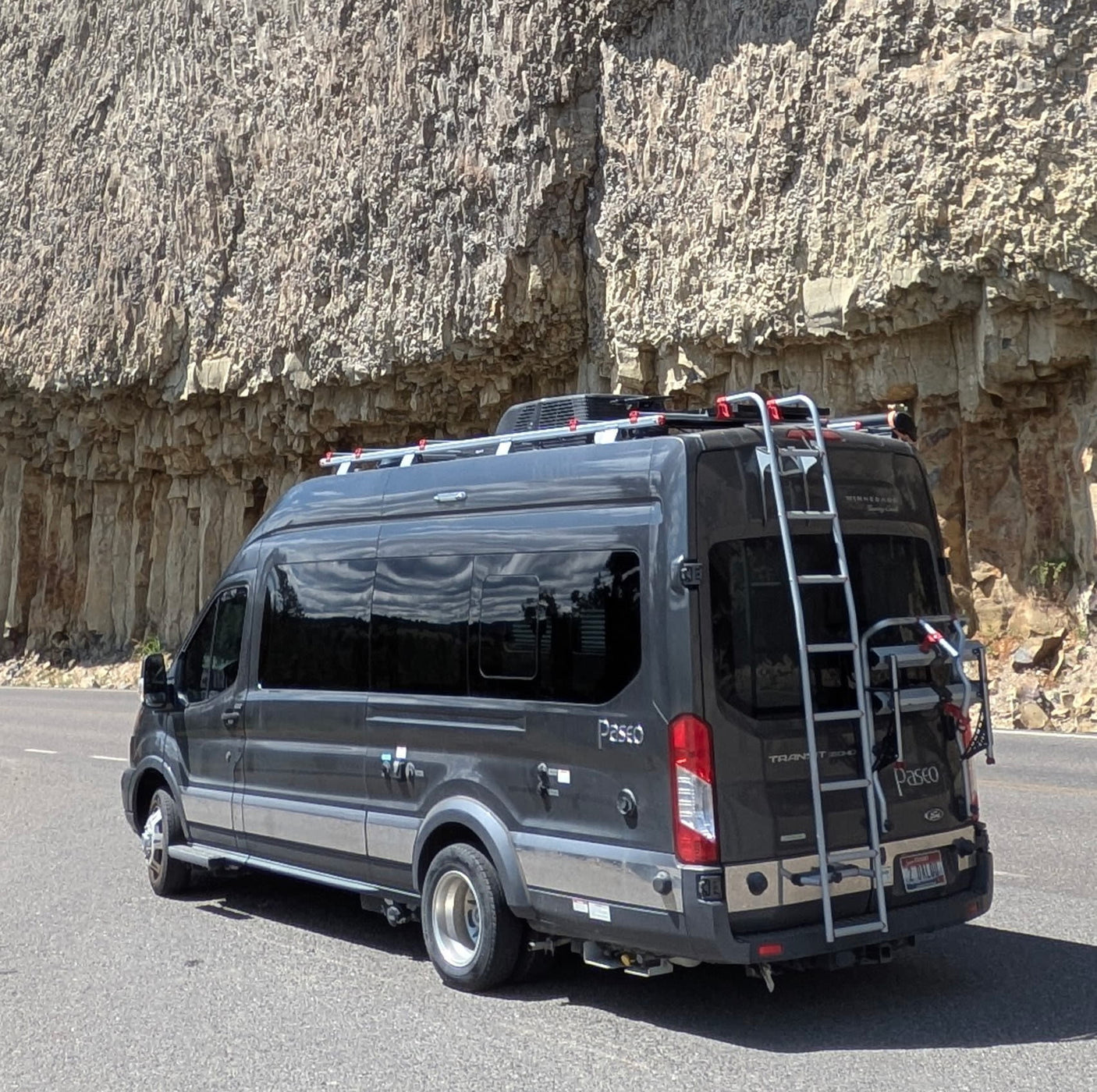 equipped as a modern camper van for adventures.|Dark gray Winnebago Paseo RV rental with roof rack & bike carrier