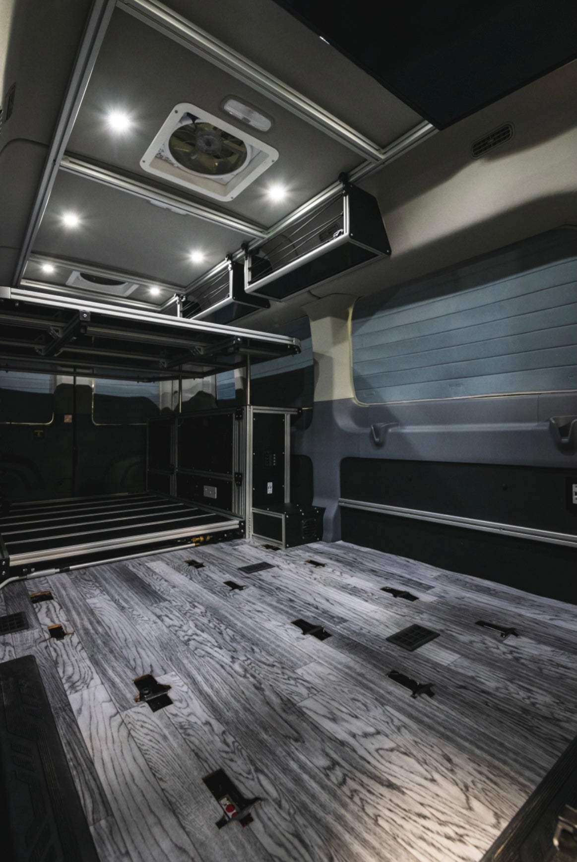 Modern RV rental interior: wood-look floor, elevated bed platform, overhead storage, and bright LED lighting.