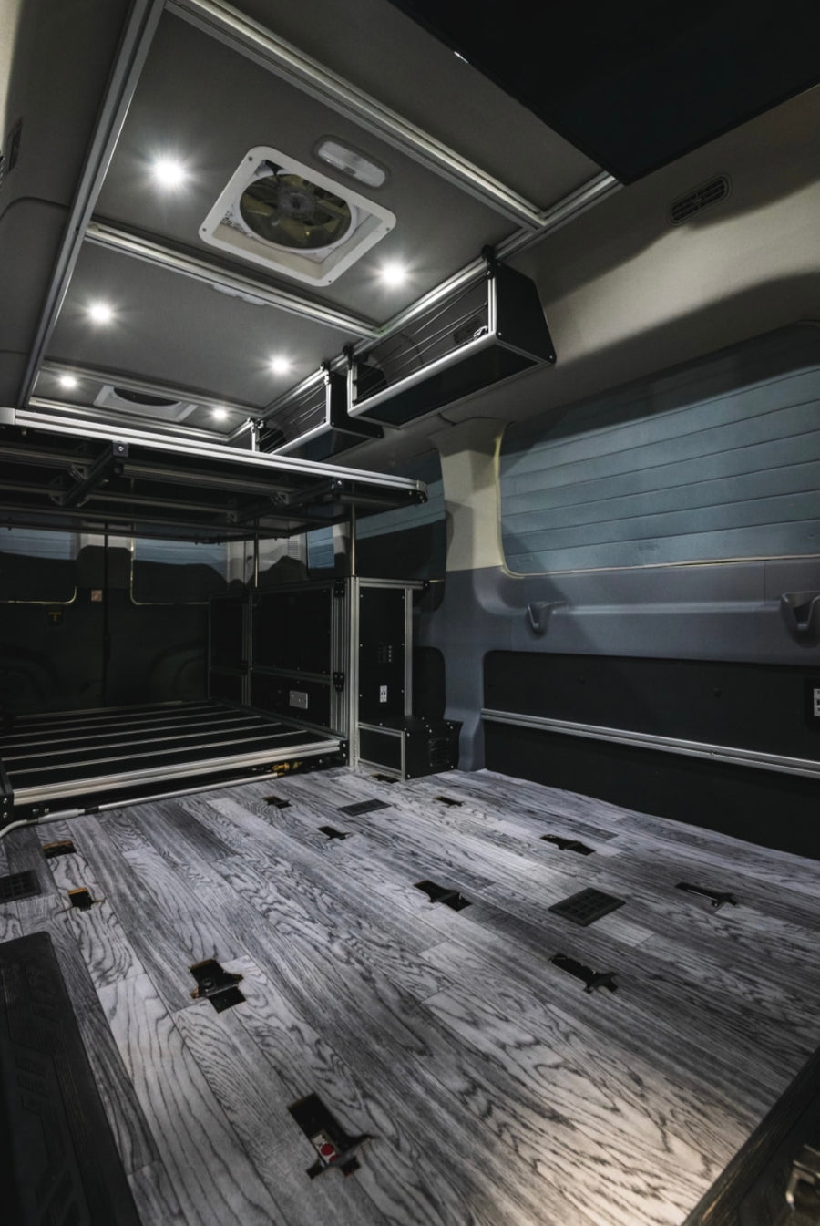 Modern RV rental interior: wood-look floor, elevated bed platform, overhead storage, and bright LED lighting.