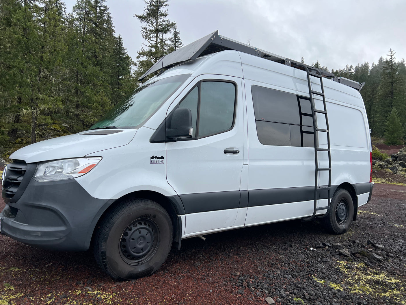 White Mercedes Sprinter campervan rv rental with roof solar and ladder, ready for adventures on a rocky trail.