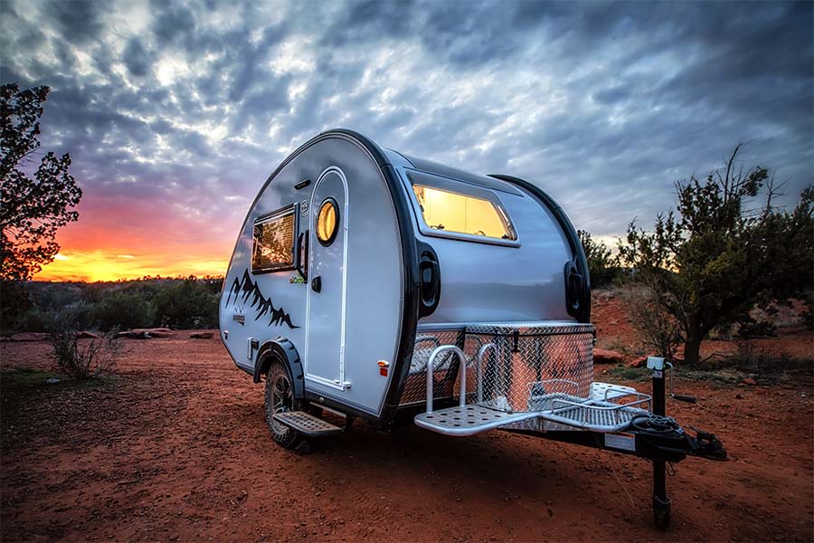 Experience the outdoors! Silver teardrop RV rental parked on red dirt at a vibrant sunset