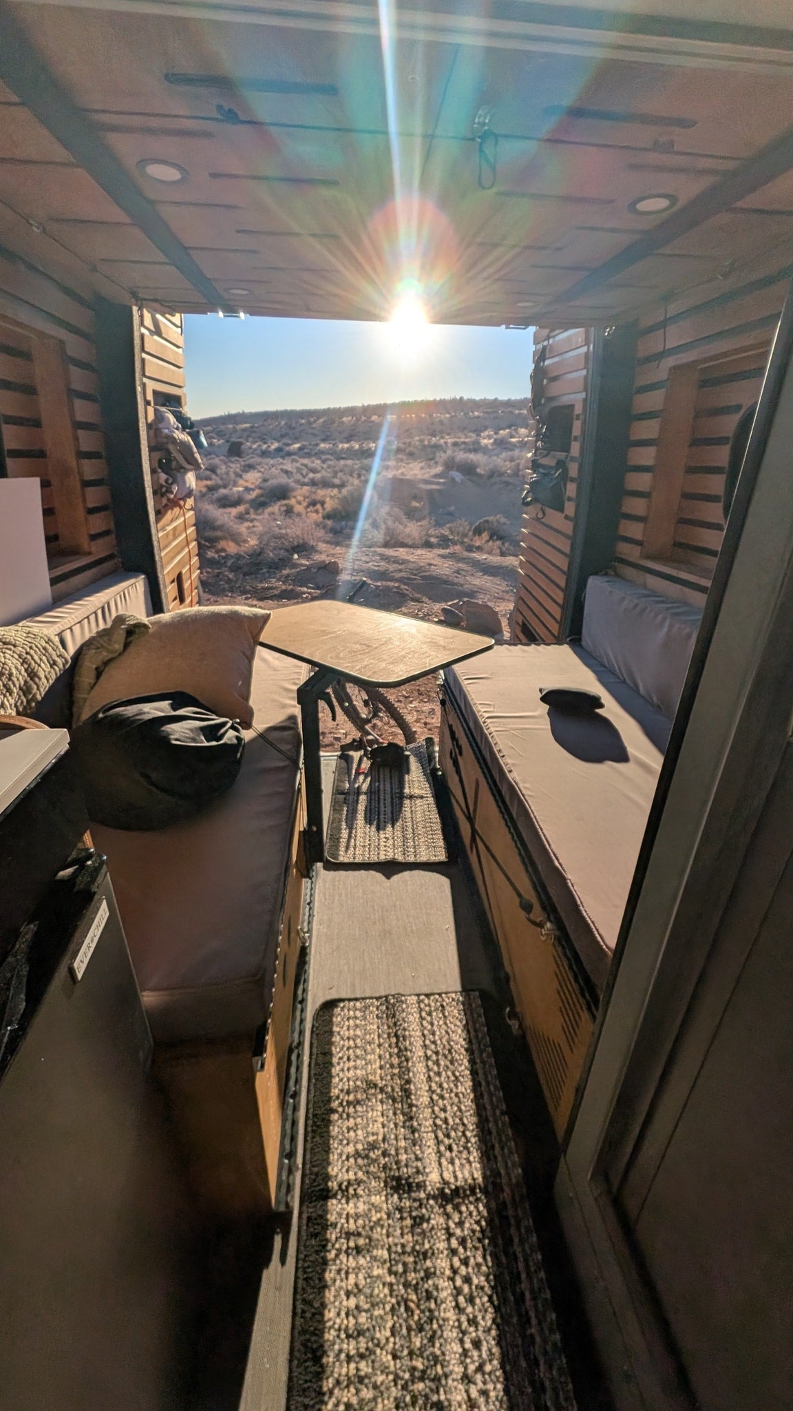 Warm desert sunset view from an RV rental interior, featuring comfy benches, a central table, and ceiling lights in a cozy camper van. — photo 3