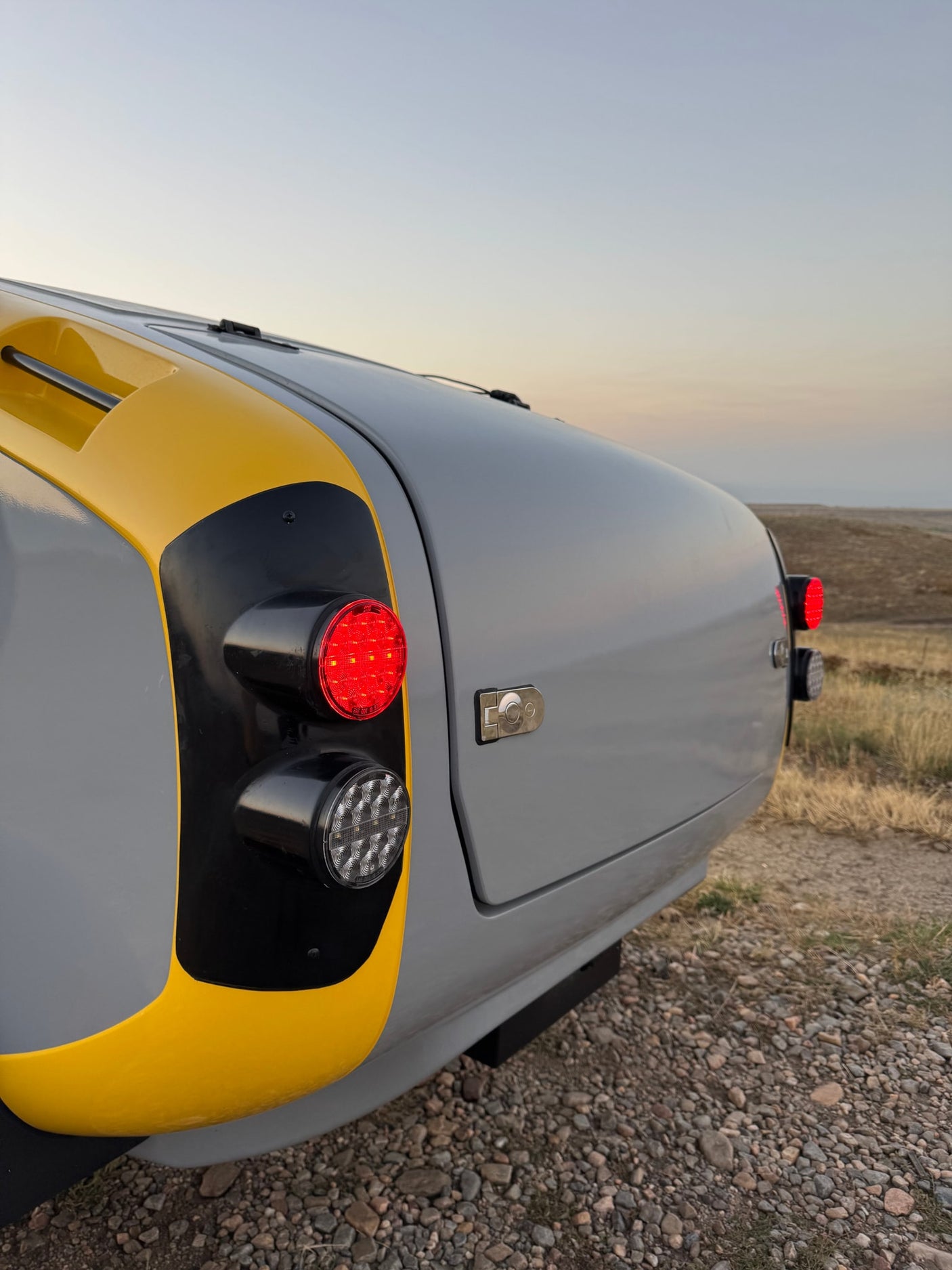 Close-up: rear of a gray and yellow teardrop RV rental with bright LED rear lights. Perfect for your next road trip!