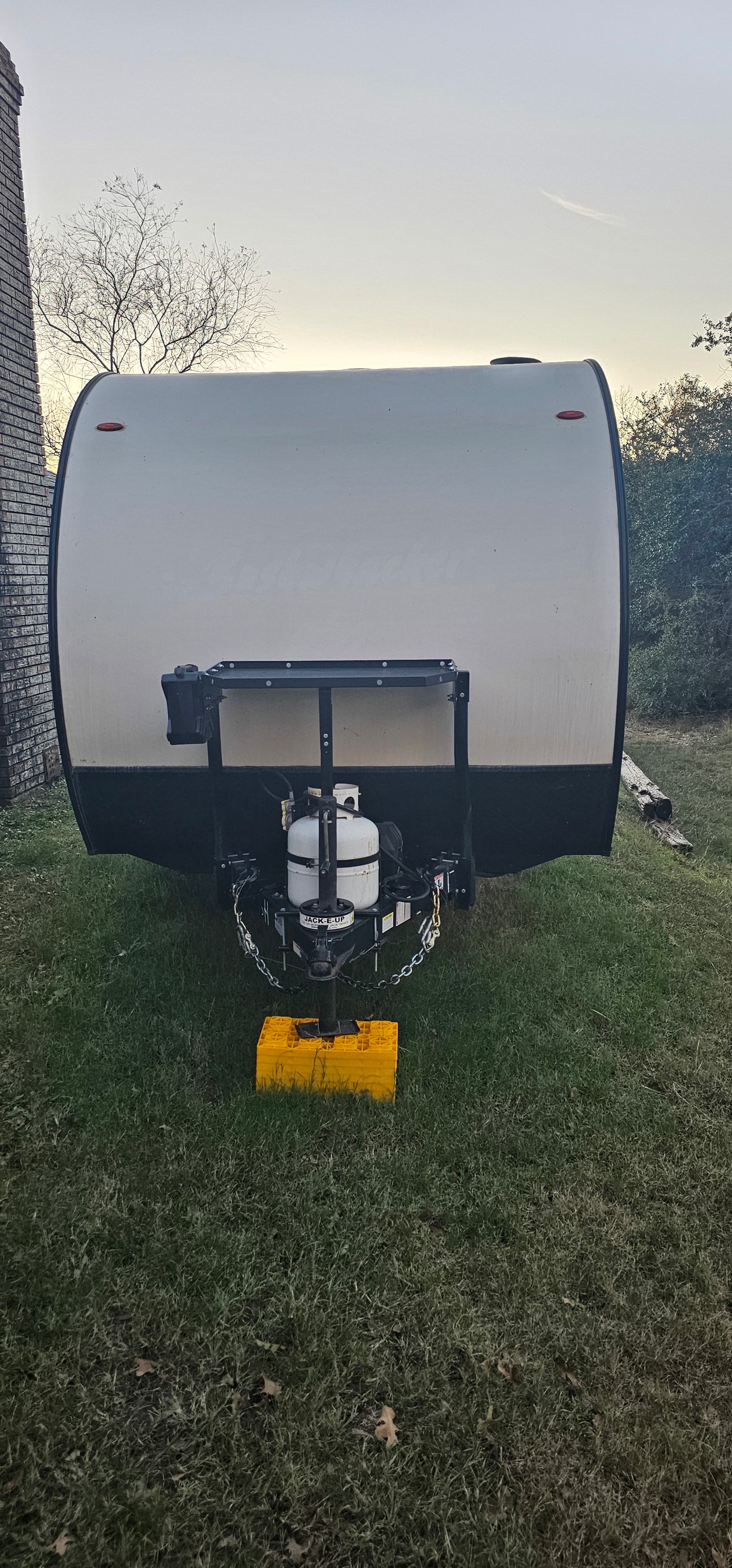Front view of an RV rental travel trailer with its propane tank and hitch, parked on grass at dusk.
