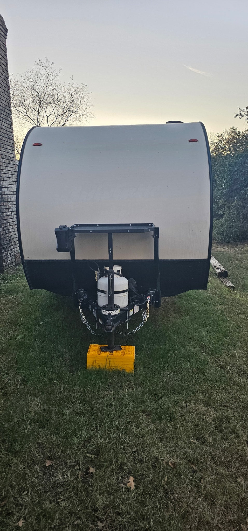 parked on grass at dusk.|Rear view of a white Texas travel trailer (RV rental) parked on green grass