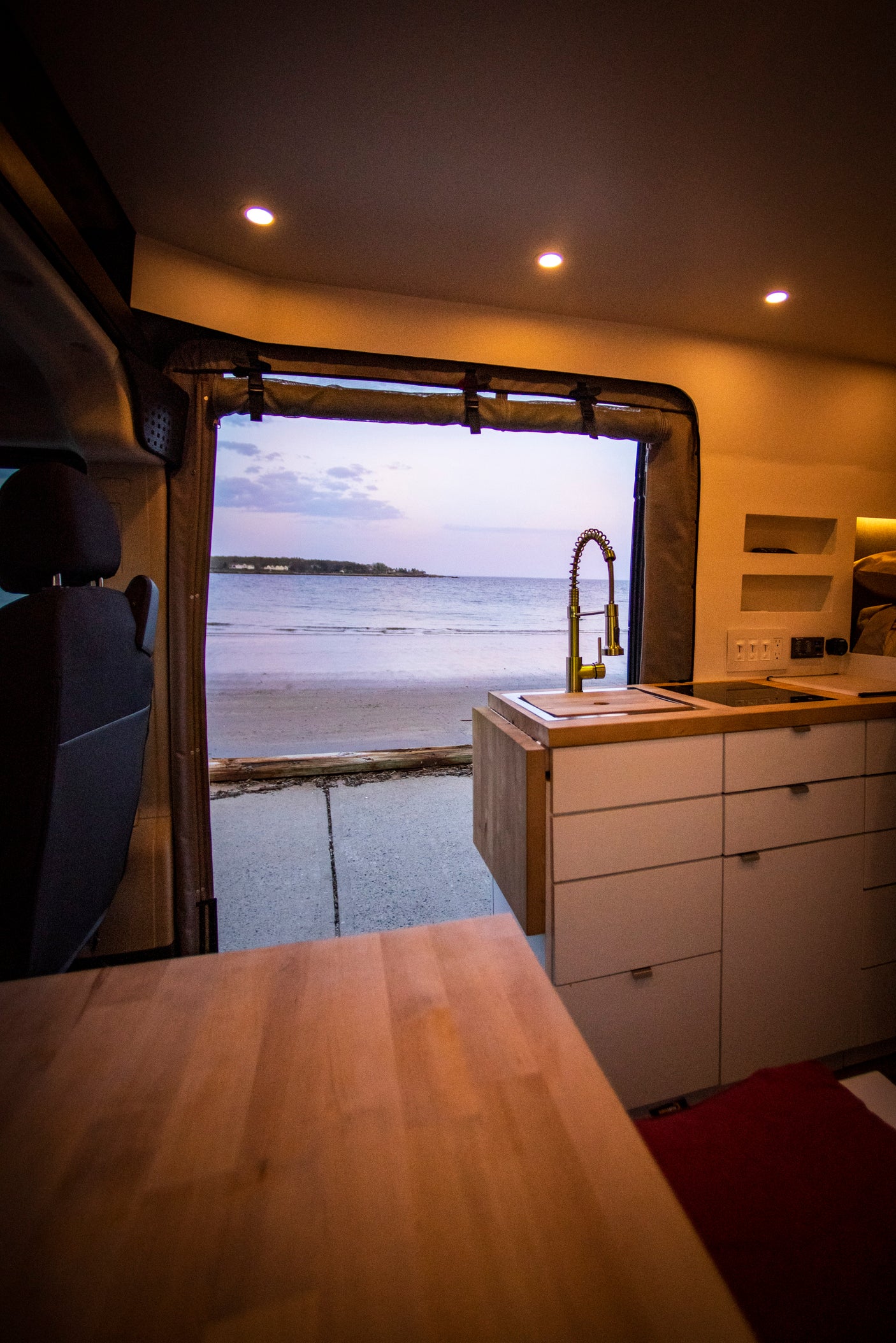 Experience an RV rental: a camper van kitchen with a stunning beach and ocean view at sunset.