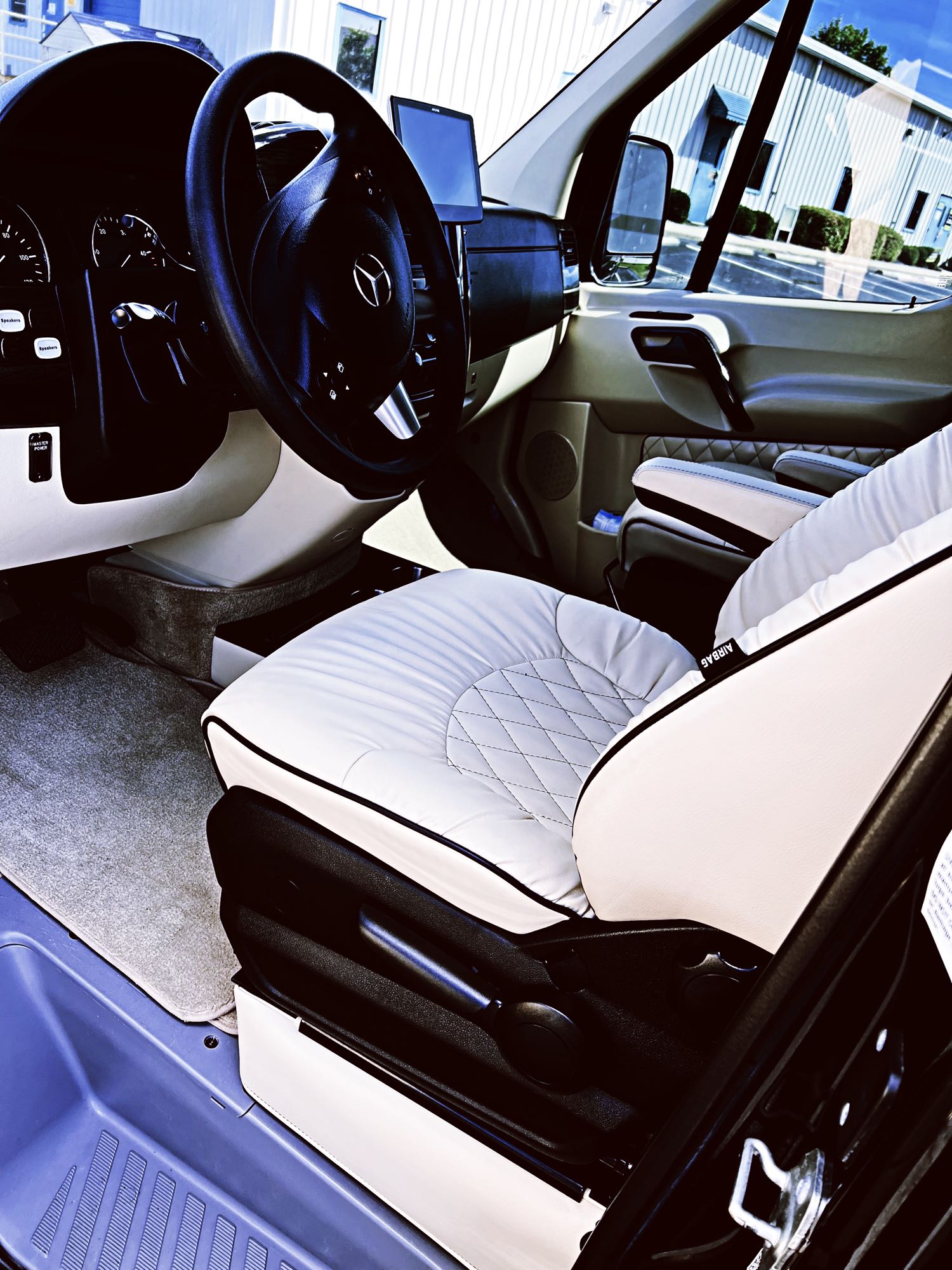 cream quilted leather seats facing each other. Perfect for travel comfort.|Experience premium travel in this RV rental! Plush tan leather seats with plaid pillows & dark wood interior offer ultimate comfort.|Luxury RV rental interior with overhead screen