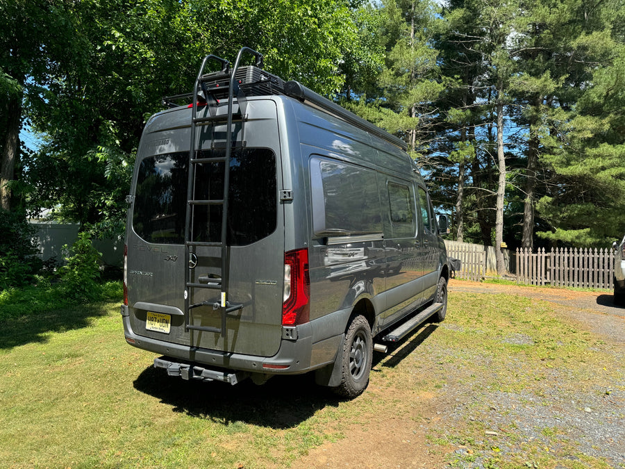 A gray Winnebago Revel Sprinter 4x4 RV with roof rack and ladder, perfect for rv rental trips, parked outdoors.