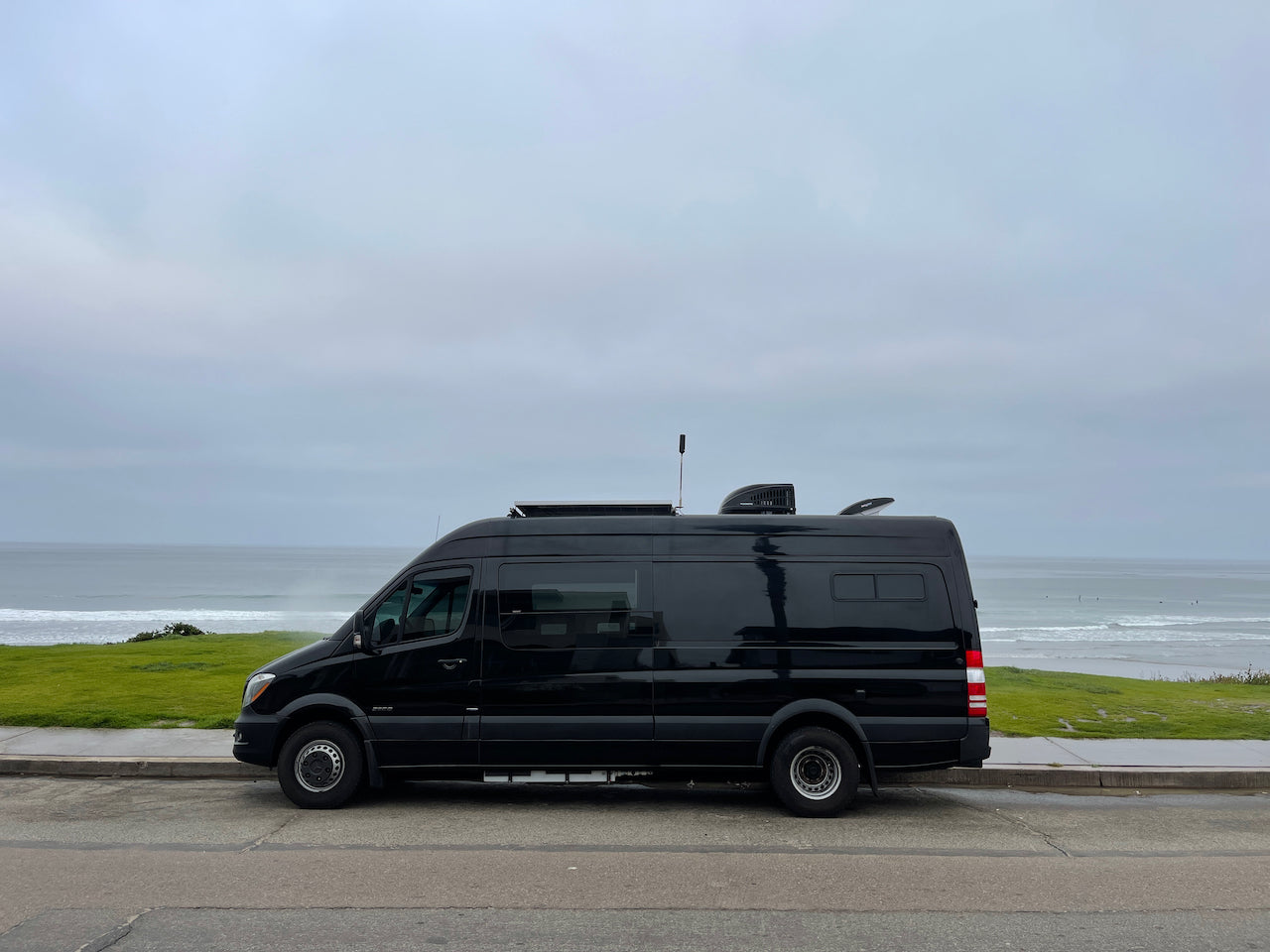 A black camper van RV rental is parked by the ocean on an overcast day, ready for adventure.